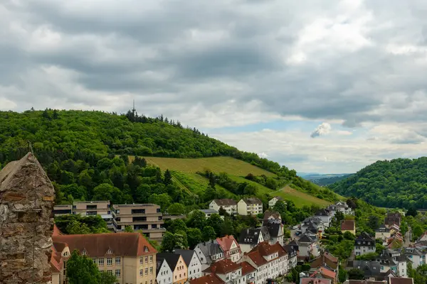 Etkileyici yeşil tepelerin eteklerine kurulmuş, dramatik bulutlu gökyüzünün altında geleneksel binalarla süslenmiş tuhaf bir köy manzarası gözler önüne seriliyor..