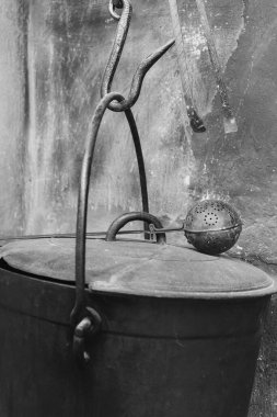 Sağlam bir kancayla asılmış yıpranmış demir bir kova, eski bir duvara dayanmış, karmaşık detaylar sergiliyor ve geçmişin hikayelerini fısıldayan antika bir tılsım..