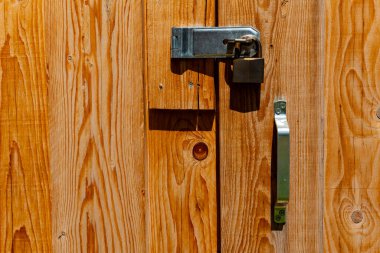 Sağlam ahşap kapı, parlak bir asma kilit ve parlak metalik bir sapla derin tahıl desenleri sergiliyor. Güneş ışığı, sahnenin kırsal çekiciliğini arttırmak için sıcak renkler bırakır..