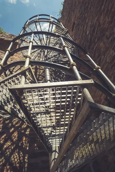 Sağlam metalden yapılmış spiral bir merdiven engebeli taş yapının içinde sarmal bir şekilde yükseliyor, parlak bir gökyüzünün altında geçmişin hikayelerini fısıldayan duvarlarla çevrili..