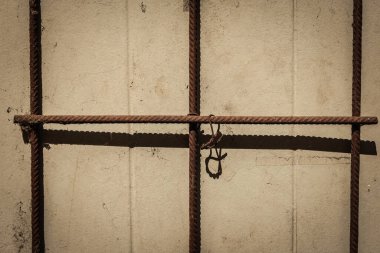 Yıpranmış metal çubuklar, güneşli bir duvarda karmaşık gölgeler oluşturarak, öğleden sonra sakin bir anda, engebeli doku ve yumuşak ışık arasındaki zıtlığı vurgular..