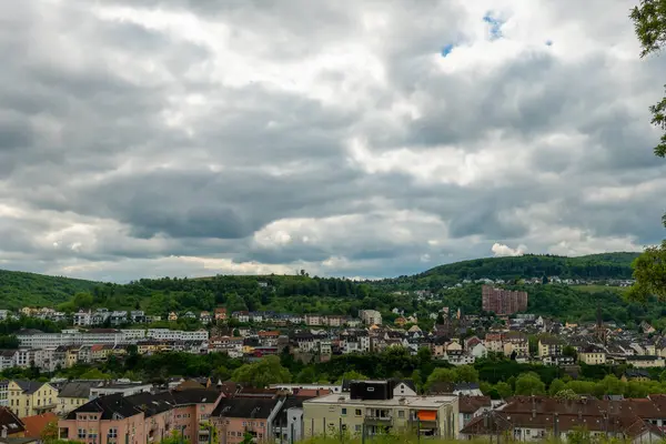 Fırıl fırıl dönen bulutlarla dolu bir gökyüzünün altında yuvarlanan yeşil tepelerin arasına yerleştirilmiş pitoresk bir kasaba ortaya çıkıyor. Hareketli binalar manzarayı dolduruyor, barışçıl bir geri çekilme yaratıyor..