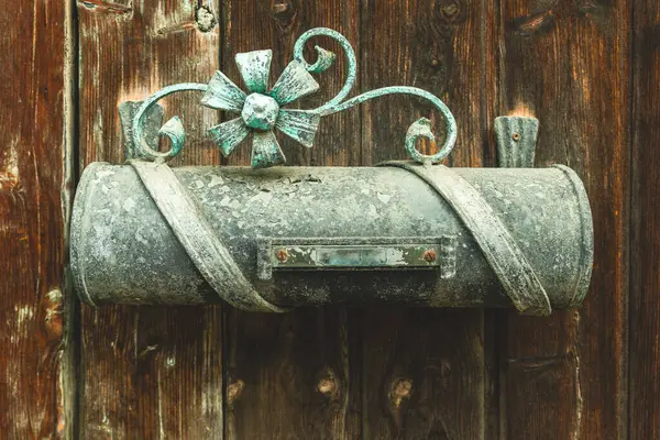 Karmaşık metal tasarımlar içeren güzel bir antika posta kutusu kırsal ahşap bir duvara monte edilmiştir. Yıpranmış ahşap ve posta kutusunun zarafeti nostaljik bir ortam yaratır..