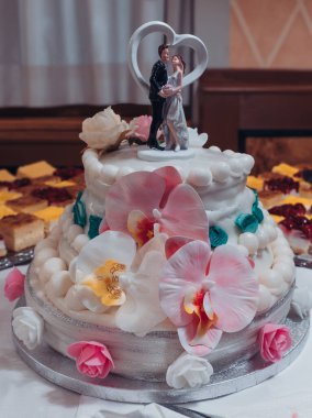 Göz kamaştırıcı bir düğün pastası canlı bir resepsiyonda gururla duruyor. Zarif şeker çiçekleri ve büyüleyici bir çiftle birlikte. Etrafını saran tatlı şeyler, şenlikli atmosferi güçlendiriyor..