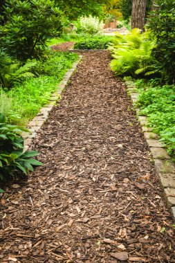 Malçtan yapılmış güzel bir yol, ziyaretçileri çevresindeki yemyeşil bahçeyi keşfetmeye davet ediyor. Canlı yeşil eğreltiotları ve çiçekli bitkiler kenarlarda, sakin bir atmosfer yaratıyor..