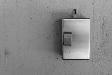 Pürüzsüz metal bir şalter, yumuşak ışıklandırmayla zarif bir şekilde aydınlatılmış dokulu bir duvara dayanıyor. Malzemelerin karışımı odada minimalist ama davetkar bir atmosfer yaratıyor..