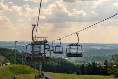 Sandalyeler canlı yeşillikler ve uzak tepelerle çevrili halatı sorunsuzca yüzdürüyor. Karamsar bulutlar yaklaşan değişime işaret ediyor, bu dağ çekilmesinin pitoresk cazibesini artırıyor..