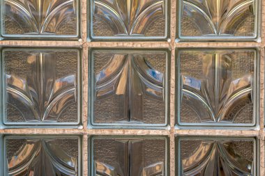 Dekoratif cam tuğla duvarın yakın plan görüntüsü. Karmaşık desenler ve dokular sergiliyor. Güneş ışığı, uzayın atmosferini arttıran sıcak yansımalar oluşturarak filtreler..