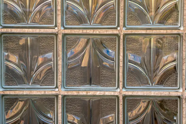 Dekoratif cam tuğla duvarın yakın plan görüntüsü. Karmaşık desenler ve dokular sergiliyor. Güneş ışığı, uzayın atmosferini arttıran sıcak yansımalar oluşturarak filtreler..