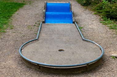 Benzersiz bir mini golf deliği oyuncuları neşeli şekli ve canlı mavi rampası ile davet eder. Yeşilliklerle çevrili bu yer güneşli bir günde eğlence ve rahatlama sunuyor..