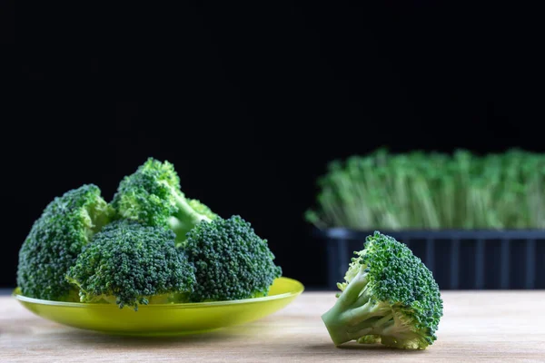 Still life organic ripe broccoli fresh vegetable on green plate on wooden background. Micro greens plant cabbage brassica oleracea germination on black background. Healthy nutrition and organic food.