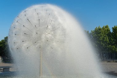 Spherical fountain spraying water in city park. Transparent splash in form ball. Fanshaped structure how dandelion blowball. Gush water and movement drops. Refreshing cool water on hot summer day.