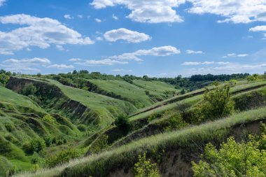 Yeşillikle kaplı vadi manzaralı. Jeolojik kusurları olan manzara vadisi. Yeryüzü dağları ve tümsekler gökyüzüne karşı rahatlıyor. Çıkıntıları ve aralıkları olan tepe kirişi. Ot ve ağaçlar bayır kanyonunda.