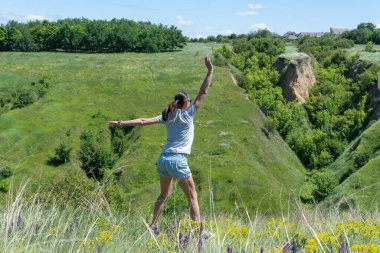 Active woman jumping on background ravine covered with greenery. Energetic young fit female showing movement jump. She carefree rises up from green meadow. Dynamic life freedom adult. Landscape valley