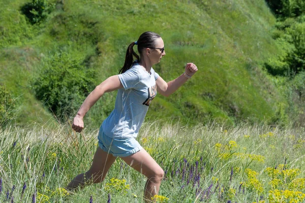 Active woman running on background ravine covered with greenery. Energetic young fit female showing movement exercising of run. She shows healthy lifestyle on green meadow. Dynamic life freedom adult.