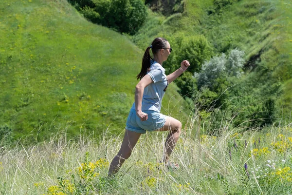 Active woman running on background ravine covered with greenery. Energetic young fit female showing movement exercising of run. She shows healthy lifestyle on green meadow. Dynamic life freedom adult.