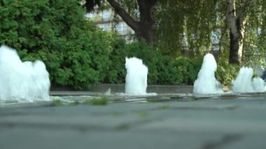 Pedestrian çeşmesi güneşli bir havada şehirde şelale gibi akıyor. Yeşil yeşillik arka planında hareket şeffaf sıçrama. Sıvı damlalardan oluşan ışıl ışıl bir su. Sıcak bir günde serinletici..