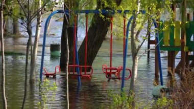 Bahar zamanı nehir kıyısında sel. Şehirde su dolu oyun ve spor alanları. Batık ağaçlarla dolu bir nehir. Şişe kıyı şeridi akışı ve doğal afet. İklim değişikliği ve ekolojik sorun.