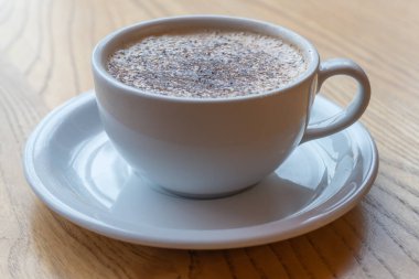 Ahşap platformda nefis bir raf kahvesi. Kafede sıcak içecekle dolu bir fincan ve çay tabağı. Kahve buğulanmış, kremalı ve ezilmiş çikolatalı..