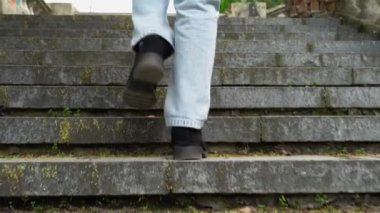 Kot pantolonlu kadın bacakları eski merdivenlerin arkasında yürüyor. Siyah süet ayakkabılı kadın ayağı adım adım eski klasik balustrade 'a çıkıyor. Ayaklar geliyor ve tırmanıyor. Bozuk merdiven ve taş korkuluklar