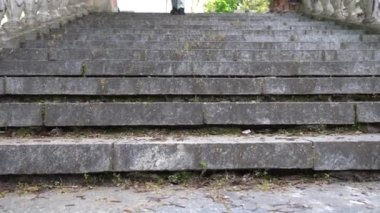 Kot pantolonlu kadın bacakları antik merdiven manzarasında yürüyor. Siyah süet ayakkabılı kadın ayağı adım adım eski klasik balustrade 'ın üzerine düşüyor. Ayaklar geliyor ve aşağı iniyor. Bozuk merdiven ve taş korkuluklar.