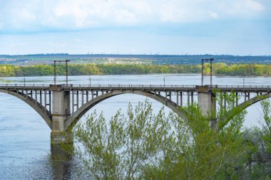 Dnepr Nehri ve demiryolu antik kemerli köprü manzarası. 19. yüzyılın geniş sularında eşsiz bir yapı. Merefo-Kherson köprüsü boyunca demiryolu hattı. Modern şehir ve bahar manzarasında panoramik.