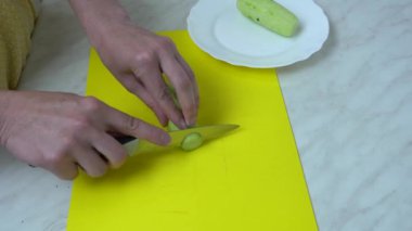 Ev hanımı mutfak bıçağıyla salatalık kesiyor. Kadın elleri mutfak tahtasındaki yeşil sebzeleri dilimliyor. Taze sebze salatası pişiriyorum. Organik vejetaryen ev yapımı yemekler. Ham vitamin diyeti.