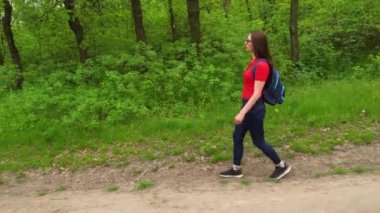 Sırt çantalı turist kadın yaprak döken ormanda yürüyor. Yeşil Vadi 'de aktif bir yetişkin yürüyüşü. Gezgin şehvetin ve bahar çimenli tepenin tadını çıkar. Kadın yürüyüşçü vahşi hayatı keşfediyor..