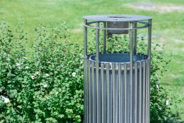 Parkta şık bir çöp kutusu. Temiz çevre için modern çöp tenekesi. Şehrin sokaklarında metal çelik çöp tenekesi. Dışarıdaki çöp bidonunu tasarla. Bahçede temizlik ve düzenlilik var. Doğa içindir..