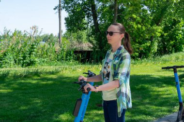 Tasasız kadın parkta kiralık elektrikli scooterla gezer. Rıhtımsız yolda giden genç bir yetişkin. Elektrikli araçta günlük kıyafetleri olan biri. Ekolojik seyahat ve macera.