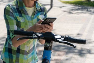 Cep telefonu olan kadın, elektrikli scooter kiralama için QR kodunu tarıyor. Akıllı telefonda limansız ulaşımı açmak için uygulamayı kullanan bir kadın. Kentsel tarzda ekolojik araç kullanmak. Modern teknolojiler.