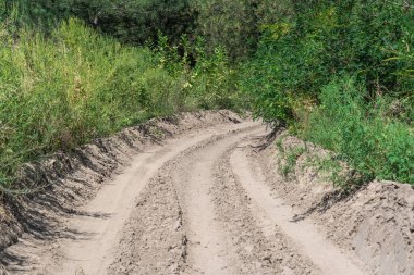 Ormandaki kum yolu. Garaj yolundaki dört tekerlekli bisikletin lastik izi. Doğa arazisindeki dörtlü bisikletin izi. Kum dokusu bozuk. Ormanda yol kapalı. Güneşli bir günde kum tepeleri ve yeşil orman.