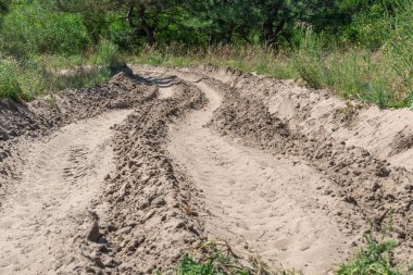 Ormandaki kum yolu. Garaj yolundaki dört tekerlekli bisikletin lastik izi. Doğa arazisindeki dörtlü bisikletin izi. Kum dokusu bozuk. Ormanda yol kapalı. Güneşli bir günde kum tepeleri ve yeşil orman.