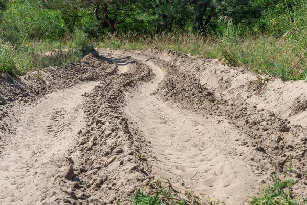 Ormandaki kum yolu. Garaj yolundaki dört tekerlekli bisikletin lastik izi. Doğa arazisindeki dörtlü bisikletin izi. Kum dokusu bozuk. Ormanda yol kapalı. Güneşli bir günde kum tepeleri ve yeşil orman.