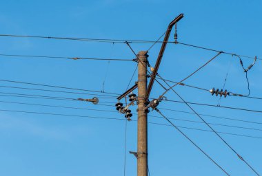 Mavi gökyüzü arka planında elektrikli demiryolu direği. Demiryolu boyunca sütunlardaki elektrik hatları. Katenareri kablo teknolojisi. Voltaj sisteminin detaylı yapısı. Demiryolu Ekipmanı.