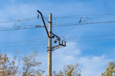 Mavi gökyüzü arka planında elektrikli demiryolu direği. Demiryolu boyunca sütunlardaki elektrik hatları. Katenareri kablo teknolojisi. Voltaj sisteminin detaylı yapısı. Demiryolu Ekipmanı.