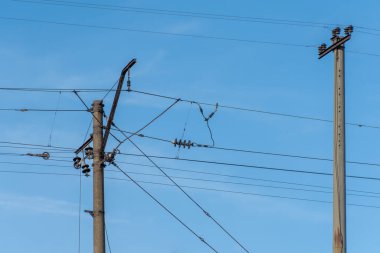 Mavi gökyüzü arka planında elektrikli demiryolu direği. Demiryolu boyunca sütunlardaki elektrik hatları. Katenareri kablo teknolojisi. Voltaj sisteminin detaylı yapısı. Demiryolu Ekipmanı.