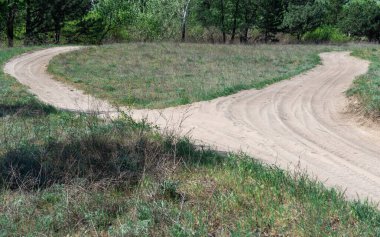 Ormandaki kum yolu. Doğa arazisindeki dörtlü bisikletin izi. Garaj yolundaki dört tekerlekli bisikletin lastik izi. Kum dokusu bozuk. Ormanda yol kapalı. Güneşli bir günde kum tepecikleri ve yeşil bitkiler.