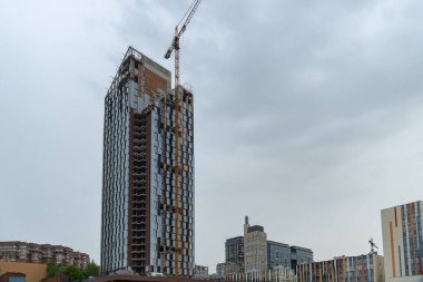 Endüstriyel inşaat vinçleri yeni modern binanın üzerinde çalışır. Beton blok ve çakışmadan oluşan çok katlı mühendislik tasarımı. Pencereler ve balkonlar için yeri olan yüksek katlı bir daire.