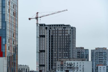 Endüstriyel inşaat vinçleri yeni modern binanın üzerinde çalışır. Beton blok ve çakışmadan oluşan çok katlı mühendislik tasarımı. Pencereler ve balkonlar için yeri olan yüksek katlı bir daire.