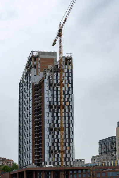 stock image Industrial construction cranes work above new modern building. Engineering multistory design from concrete block and overlap. Development high-rise apartment with place for windows and balconys.