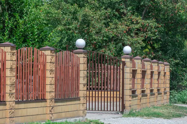 stock image Fence with wooden panels and brick wall on yard grounds. Brown straight picket fence and light surrounding wall in outdoors. Hard material painted wood stain. Featheredge garden fence with concrete.