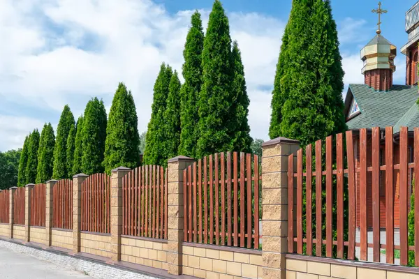 stock image Fence with wooden panels and brick wall on yard grounds. Brown straight picket fence and light surrounding wall in outdoors. Hard material painted wood stain. Featheredge garden fence with concrete.