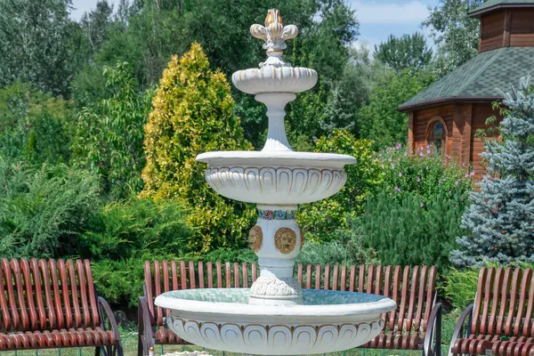 stock image White three-tiered fountain on church grounds. Painted patterns on falling water object in public park. Stone material and design fountain details on built structure. Famous place of leisure activity.