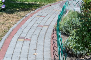 Yeşil çit boyunca taştan yapılmış bahçe yolu. Kaldırımda kaldırım taşları parktaki çiçek tarlaları arasında kıvrılıyor. Botanik bahçesinde süslü yaya geçidi var. Asfalt doğal taştan yapılmıştır..