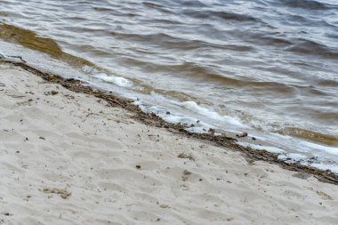 Dalgalar ve beyaz köpüklü nehir kıyısı. Beyaz yumuşak köpük sallanıyor. Kumlu sahilde mavi su kenarında. Sığ sularda doğal girdap. Plajın sakin manzarası.