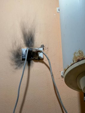 Bu fotoğraf, duvarında siyah is olan yanmış bir elektrik prizi gösteriyor. Bu da kısa devre ya da elektrik yangınını gösteriyor. İki kablo hala takılı, önemli bir güvenlik tehlikesini vurguluyor