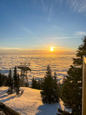 A scenic view of Skyride Gondola at The Peak of Vancouver above the White Puffy Clouds at sunset clipart