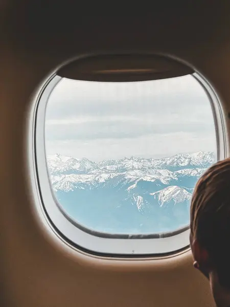 stock image A boy looking out of an airplane window at a stunning view of snow-capped mountains below, blending the excitement of travel with the beauty of nature