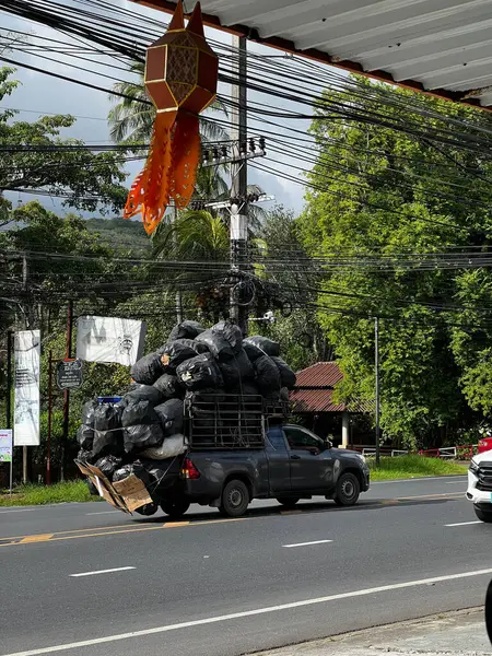 Phuket, Tayland-15 Kasım 2023: Bu fotoğraf Phuket 'te çekildi, geniş siyah çantalar taşıyan aşırı yüklü bir kamyoneti gösteriyor, yemyeşil bir zemin ve karışık elektrik hatlarına karşı kurulmuş.